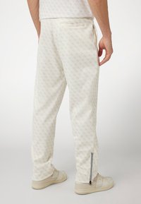 White, patterned jogger pants with a zip detail at the ankle and a back pocket. Made from a soft material with a relaxed fit.
