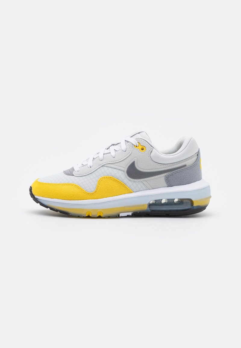 Nike Air Max-sneaker med en övervägande vit, grå och ljusgul färgschema; har andningsbart nät och en synlig luftenhet.