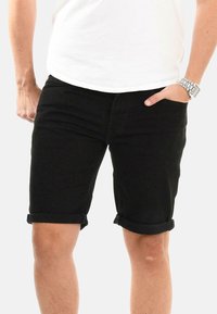 Black denim shorts featuring a straight cut, rolled cuffs, and front pockets. The fabric has a smooth texture with minimal stitching details.