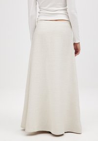 Ein langer, weißer Rock aus strukturiertem Stoff, der in einem ausgestellten Design bis zum Boden reicht und einen sauberen, gesäumten Rand hat.