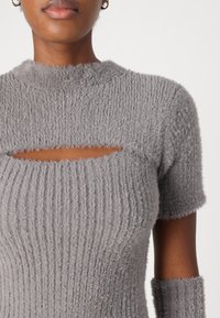 Top en maille grise avec une apparence pelucheuse et texturée. Comprend un col rond et une découpe en scoop au niveau de la poitrine. Manches courtes et design côtelé.