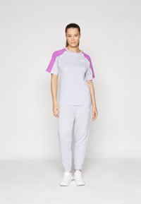 Ljust grå sportoutfit med en t-shirt med rund hals och lila ärmar samt matchande smala byxor; tillverkad av andningsbart tyg.