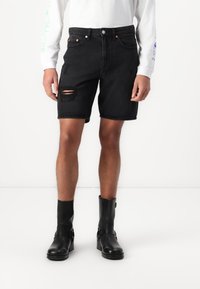 Sorte denimshorts med et slidt mønster på højre lår, med et klassisk fem-lomme-design og metalbeslag.
