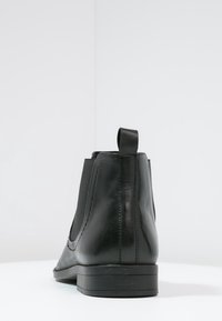 Botas de tobillo de cuero negro con paneles laterales elásticos, un acabado suave y una pequeña lengüeta en la parte posterior. Suela plana con un detalle mínimo.