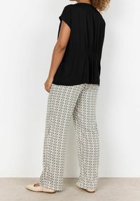 Haut noir à manches courtes avec un détail froncé dans le dos, associé à un pantalon large à motifs avec des rayures verticales et des motifs en losange beige et vert.