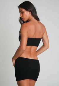 Svart stickad tvådelad set bestående av en strapless cropped topp och matchande mini kjol. Materialet har ett strukturerat mönster och en figursydd design.