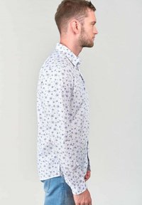 Witte shirt met een blauw bloemenpatroon, met een button-down kraag, lange mouwen en een lichte staart. Draagt het met lichtblauwe jeans.