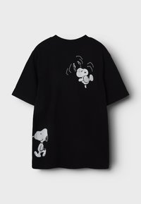 Camiseta de algodón negra con diseños de Snoopy en blanco; uno en la parte posterior y otro en el frontal cerca del dobladillo. Mangas cortas, corte relajado.