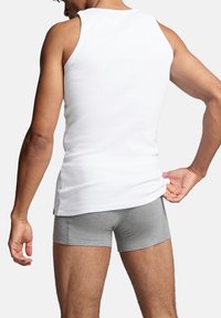 Weißes Baumwoll-Tanktop kombiniert mit grauen Boxershorts. Das Tanktop hat einen taillierten Schnitt mit Rundhalsausschnitt und ärmellosem Design, was einen lässigen Look schafft.