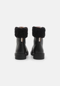 Black leather ankle boots with black fur cuffs, textured leather, and a brown and white pull tab on the back of each boot.
