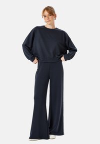 Donkerblauwe sweatshirt en wijde broek set, gemaakt van zachte stof, met een comfortabele pasvorm en contrasterende zijstrepen op de broek.