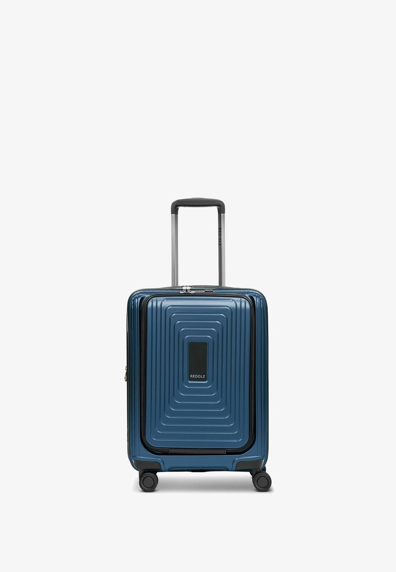 Valigia rigida blu con motivi rettangolari concentrici testurizzati, cerniera robusta, dettagli neri e manico telescopico nella parte superiore.