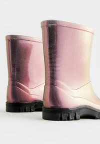 Růžové iridescentní gumové boty s texturovaným povrchem, krátká výška, zakřivené strany a černá gumová podrážka se vzory pro zajištění přilnavosti.