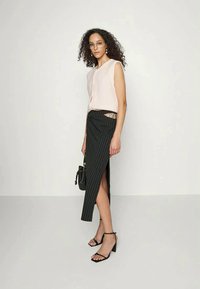 Blusa sem mangas de um rosa claro e saia escura de riscas com uma fenda alta, combinadas com saltos pretos de tiras e uma pequena bolsa.