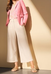 Rosa blazer med två knappar, ljusgrå mönstrad topp, beige vida byxor och guldiga sandaler med volangdetalj.