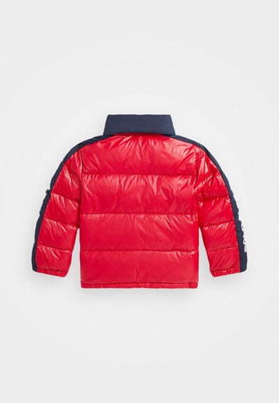 Veste rembourrée rouge avec col et manches navy, présentant une texture matelassée et un détail de logo sur la manche gauche. Conçue pour la chaleur.