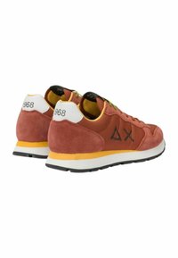 Sneaker in suede color rosso-bruno con accenti gialli, che presentano un tallone bianco, lacci verdi e un logo distintivo sui lati.