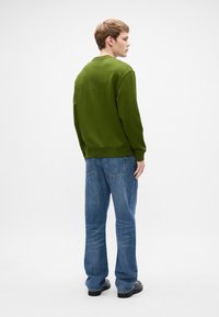 Sweatshirt verde de gola redonda com tecido texturado, punhos e cintura canelados. Combinado com jeans de ganga azuis e sapatos pretos. Vista de trás.