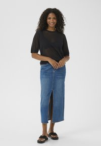 Haut noir transparent à manches courtes, jupe crayon en denim bleu avec fente à l'avant, associé à des sandales plates noires. Design simple et décontracté.