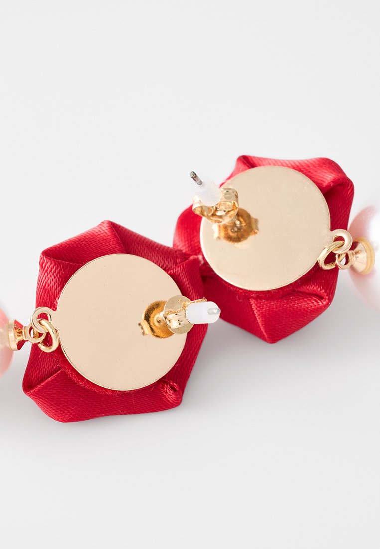 Orecchini in satin rosso con hardware dorato, caratterizzati da una base rotonda e un accento in perla lucida, che presentano un design piegato unico.