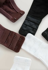 Des rallonges de soutien-gorge en noir, blanc et marron, montrant des fermetures à agrafes sur une surface claire.