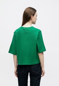 Πράσινο βαμβακερό T-shirt με κοντά μανίκια, χαλαρή εφαρμογή και λαιμόκοψη στρόγγυλη. Λείο υφές, μονόχρωμο και ελαφρώς cropped σχεδιασμό.