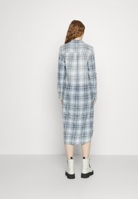 Sukienka w kratę z długim rękawem w jasnoniebieskim i białym kolorze, wykonana z lekkiego materiału. Posiada kołnierz z guzikami i długość do połowy łydki.