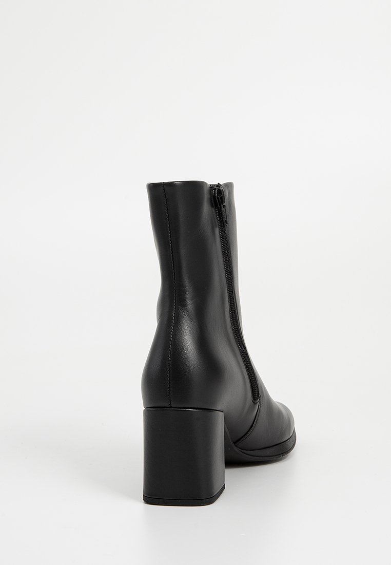 Fekete bőr bokacsizma sima textúrával, hátsó cipzárral és vastag sarkal. Egyszerű dizájn, kerek orral.