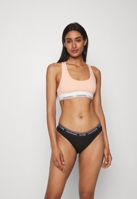 Világos rózsaszín sportmelltartó fehér Calvin Klein logós pánttal; fekete tanga fekete pánttal, rajta "CK ONE" logóval. Sima anyag, testhezálló kialakítás.