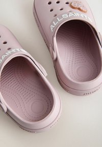 Sabots en caoutchouc roses dotés d'une semelle intérieure texturée, de trous de ventilation et d'une large bande blanche avec le logo "ALLSAINTS". Design lisse et arrondi.
