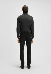 Czarne spodnie o dopasowanym kroju, zestawione z ciemnoszarym swetrem z długim rękawem. Prosty wzór, dzianinowa faktura, bez widocznych wzorów czy akcentów.