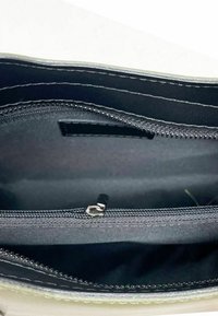 Inredning av en dragkedjeförsedd handväska i svart tyg, med en mindre dragkedjaavdelning. Kanterna är kantade i ljusare material.