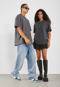 Uhlová šedá voľná tričká, modré voľné džínsy, čierne čižmy po kolená a pohodlné tenisky skombinované pre moderný streetwear štýl.