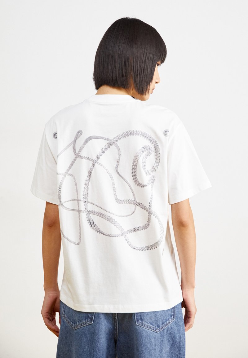 Hvid bomulds t-shirt med et sølvreb design på ryggen, afslappet pasform, korte ærmer og rund halsudskæring. Denim shorts synlige.