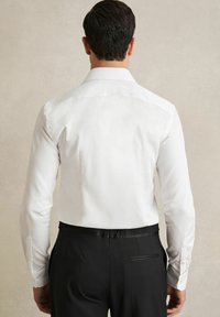 Cămașă albă cu guler structurat și mâneci lungi, asortată cu pantaloni negri care au un buzunar din spate ascuns și o talie din satin.