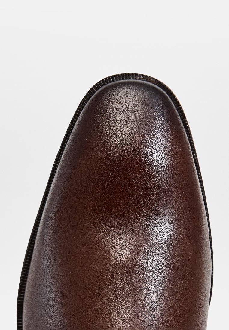 Zapato de vestir de cuero marrón con acabado suave, punta curva y un sutil borde texturizado a lo largo de la abertura. Apariencia pulida.