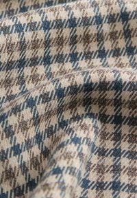 Tissu beige doux avec un motif pied-de-poule à carreaux bleu et marron texturé, montré en plis en gros plan.