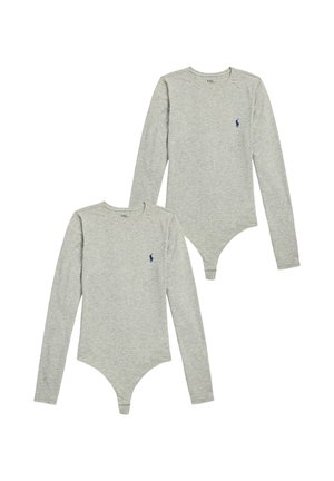 Kvinde iført en tætsiddende grå heldragt med lange ærmer, med en grå sweater bundet om taljen og cremefarvede sokker.