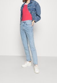 Jeans a vita alta in denim azzurro chiaro abbinati a una canotta rosa e a un giubbotto di denim cropped, completati da sneakers bianche.