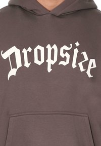 Brun hættebluse med en kontrasterende hvid grafisk tekst "Dropsize" i en stiliseret skrifttype, med en kængurulomme og almindelig pasform.