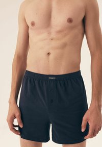 Czarne bawełniane bokserki z guzikiem, elastycznym pasem i gładką fakturą, zaprezentowane na modelu bez koszulki.