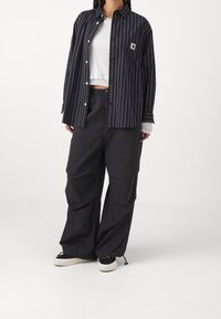 Camisa de botones a rayas blancas y negras combinada con pantalones sueltos negros. La camisa cuenta con un bolsillo en el pecho; los pantalones tienen una cinturilla elástica.