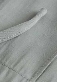 Zbliżenie na szarą pętlę z tkaniny i detal szwu na fakturowanej, tkanej tkaninie.