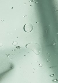 Texturiertes mintgrünes Gewebe mit unterschiedlich großen Wassertropfen, einige kugelförmig und reflektierend, die einen glatten Glanz über die Oberfläche erzeugen.