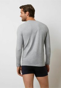 Gray long-sleeve shirt made of soft fabric, featuring a crew neck and fitted design, paired with navy shorts, viewed from the back.