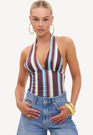 Femme aux cheveux tirés en arrière portant un haut à bretelles rayé et un jean bleu taille haute, accessoirisée de boucles d’oreilles créoles dorées et de bracelets.