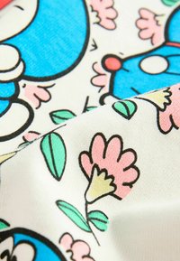 Színes textil, amely kék mesefigurákat és rózsaszín, zöld virágmintákat tartalmaz egy krém színű háttéren, textúrált felülettel.
