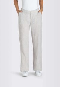 Persona che indossa pantaloni beige chiari a gamba dritta con tasche e sneakers bianche, in piedi con le mani in tasca.
