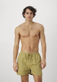 Bañador de hombre en color caqui, hecho de tejido ligero, con cinturilla elástica y cordón ajustable, y bolsillos laterales, con una textura suave.