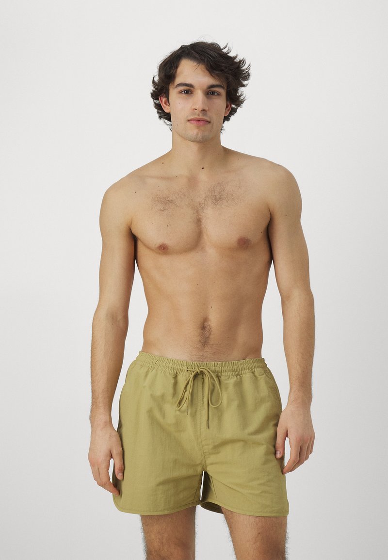 Bañador de hombre en color caqui, hecho de tejido ligero, con cinturilla elástica y cordón ajustable, y bolsillos laterales, con una textura suave.